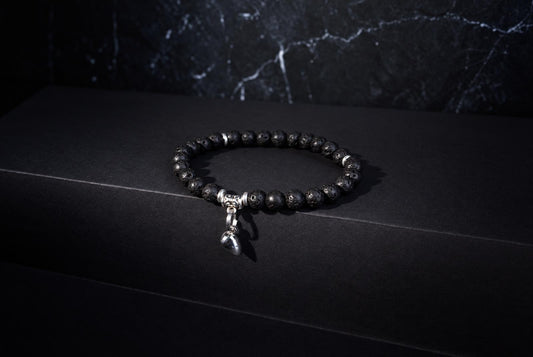 A black lava bead bracelet with silver accents and a heart-shaped charm rests on a dark surface.