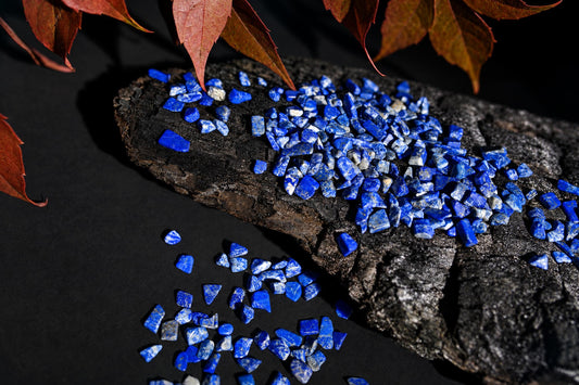 Small vivid blue stones with white patches are scattered on a dark textured surface beneath reddish leaves.