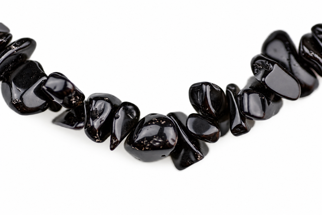 A necklace of glossy black obsidian chips arranged in a curved line on a white background.