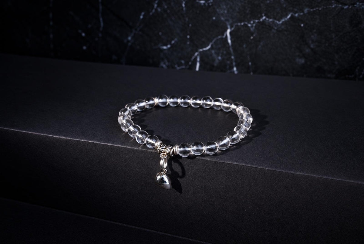 Clear round beads form a bracelet with a dangling silver-tone heart charm on a black surface.