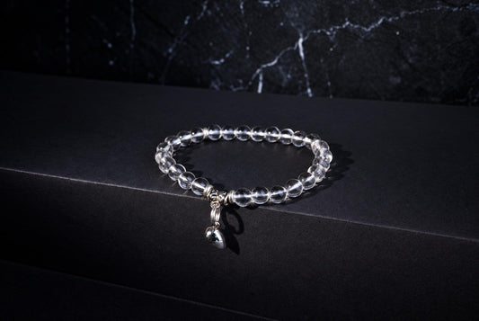 Clear round beads form a bracelet with a dangling silver-tone heart charm on a black surface.