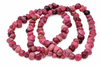 A necklace of polished rhodonite chips in shades of pink, red and dark purple arranged on a white surface.