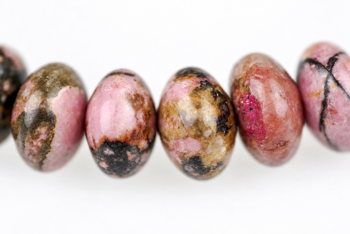 A row of polished, oval beads with pink, brown and black patterns on a white surface.