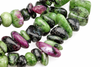 A strand of polished, tumbled chips showing green, black and pink stones on a white surface.