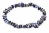 A bracelet of irregular polished blue, grey and white stone chips with brown flecks forms a loop on white.