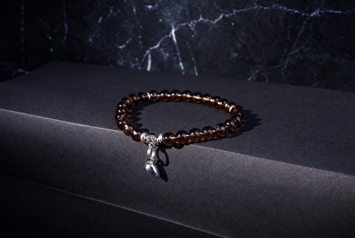 A bracelet of translucent brown round beads with a dangling silver-tone heart charm on a dark surface.