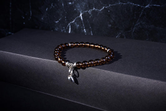 A bracelet of translucent brown round beads with a dangling silver-tone heart charm on a dark surface.