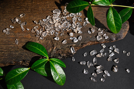 Small clear to pale brown polished stones are scattered on a wooden surface beside green leaves.