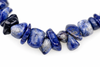 A string of polished sodalite chips in deep blue and white, arranged on a pale surface.