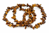 Overlapping bracelets of irregular polished golden-brown stone chips lie on a white background.