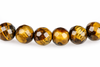 Six faceted round beads with golden brown and black stripes arranged in a row on a white surface.
