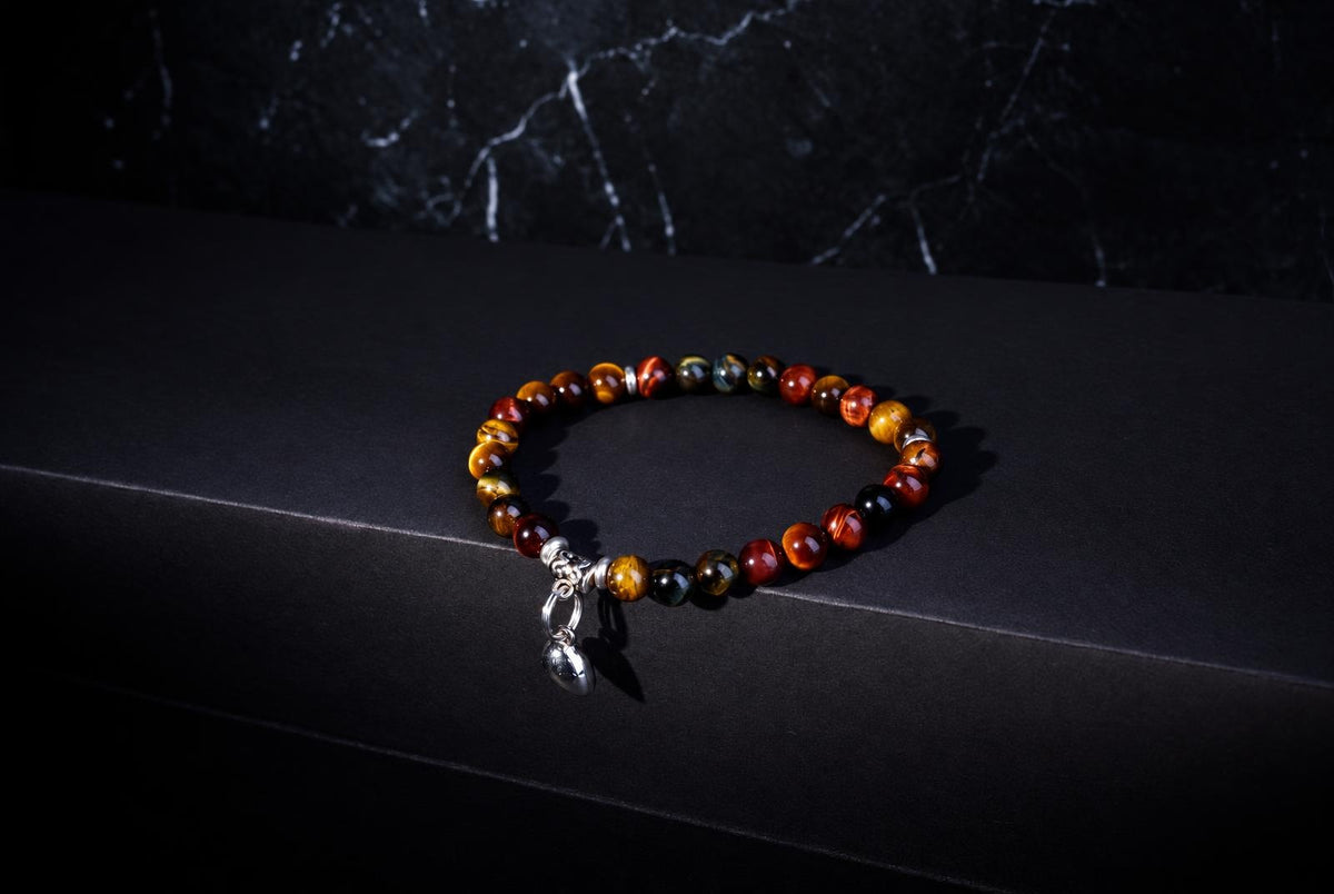 A bracelet of polished orange, brown and black round beads with a dangling silver-tone heart charm on a dark surface.