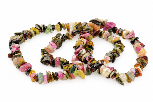 A multi-coloured tourmaline chip bracelet with pink, green, yellow and black stones arranged in a loose coil on a white surface.