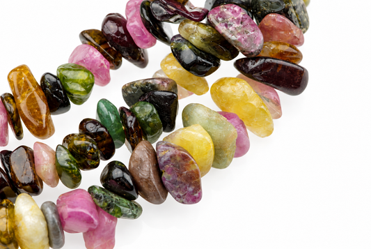 A bracelet of multi-coloured tourmaline chips in pink, green, yellow and brown on a white surface.