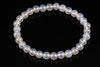 A bracelet of round, milky white beads with a subtle sheen, arranged in a circle on a dark surface.