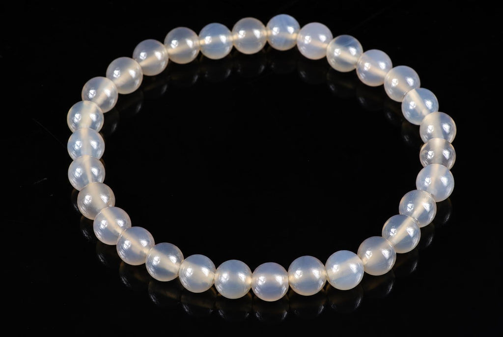 A bracelet of round, milky white beads with a subtle sheen, arranged in a circle on a dark surface.