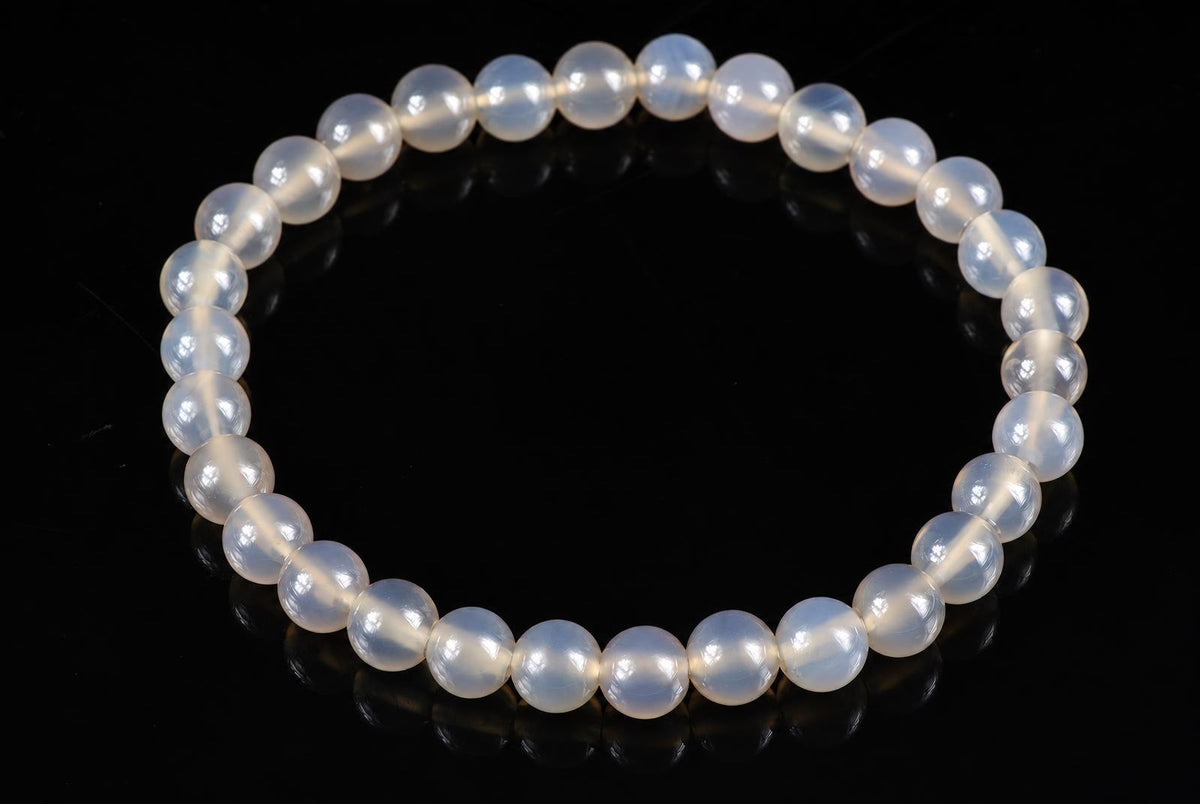 A bracelet of round, milky white beads with a subtle sheen, arranged in a circle on a dark surface.