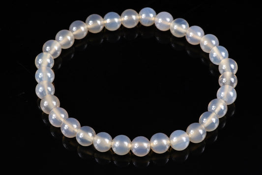 A bracelet of round, milky white beads with a subtle sheen, arranged in a circle on a dark surface.