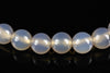 A row of round, pale white agate beads with a smooth surface on a dark reflective background.