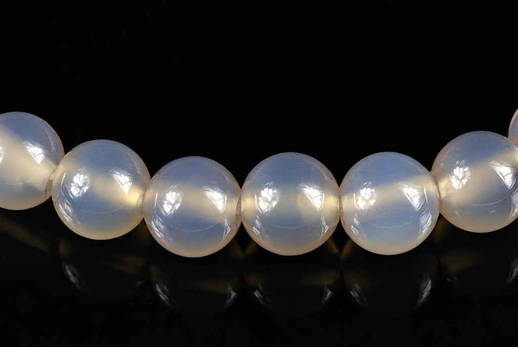 A row of round, pale white agate beads with a smooth surface on a dark reflective background.