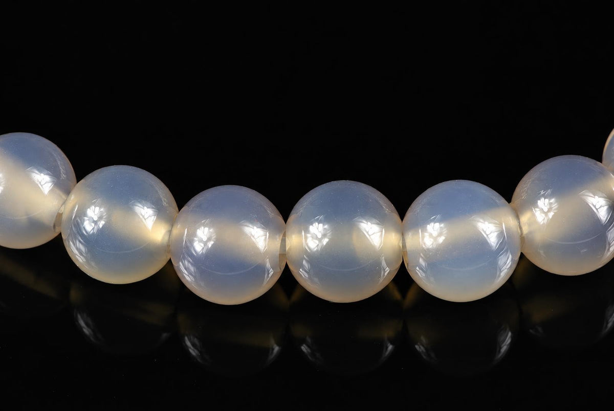 A row of round, pale white agate beads with a smooth surface on a dark reflective background.