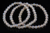 A bracelet of round, pale white beads with a subtle sheen, arranged in loops on a dark surface.