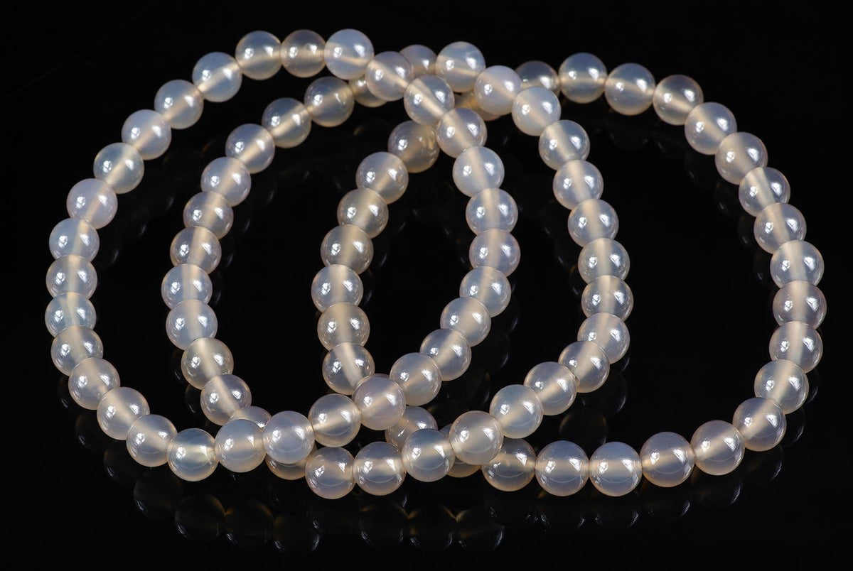 A bracelet of round, pale white beads with a subtle sheen, arranged in loops on a dark surface.