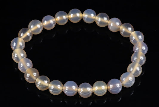 A bracelet of round, pale yellow and white agate beads with a milky sheen on a dark surface.