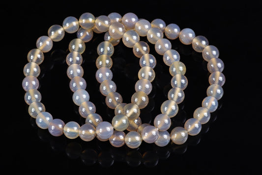 A strand of round, pale beads with a milky sheen and golden streaks lies on a dark surface.