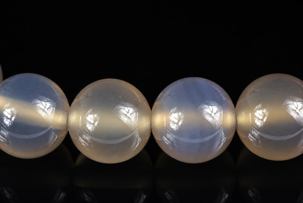 Four round agate beads with carved floral patterns, pale blue and cream tones, on a dark surface.
