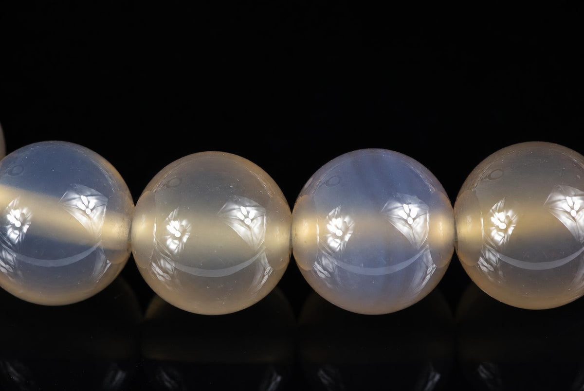 Four round agate beads with carved floral patterns, pale blue and cream tones, on a dark surface.