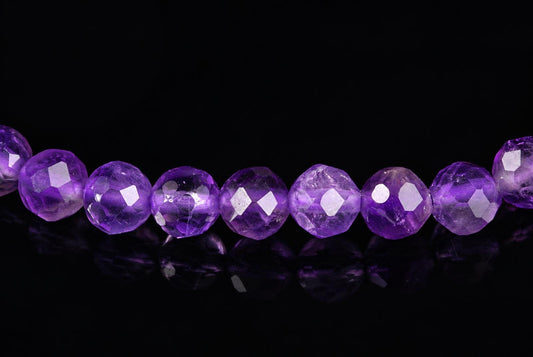 A row of faceted purple beads on a dark surface with reflections.