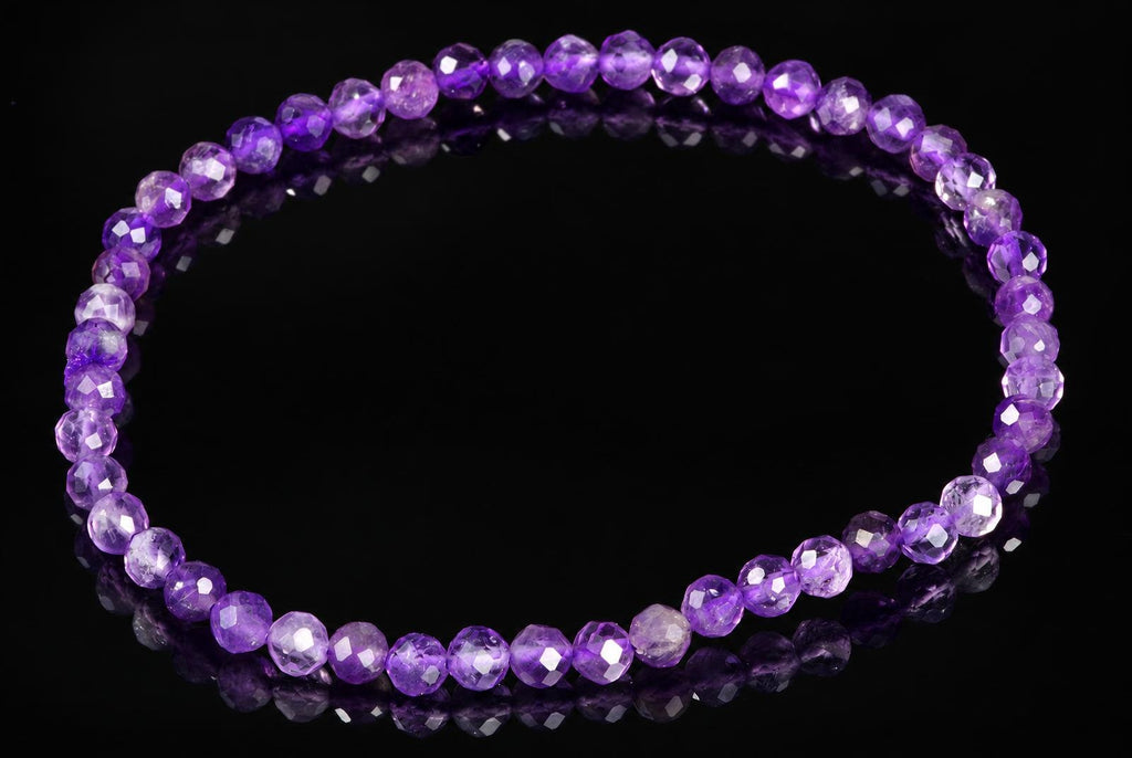 A bracelet of faceted purple beads on a dark reflective surface.