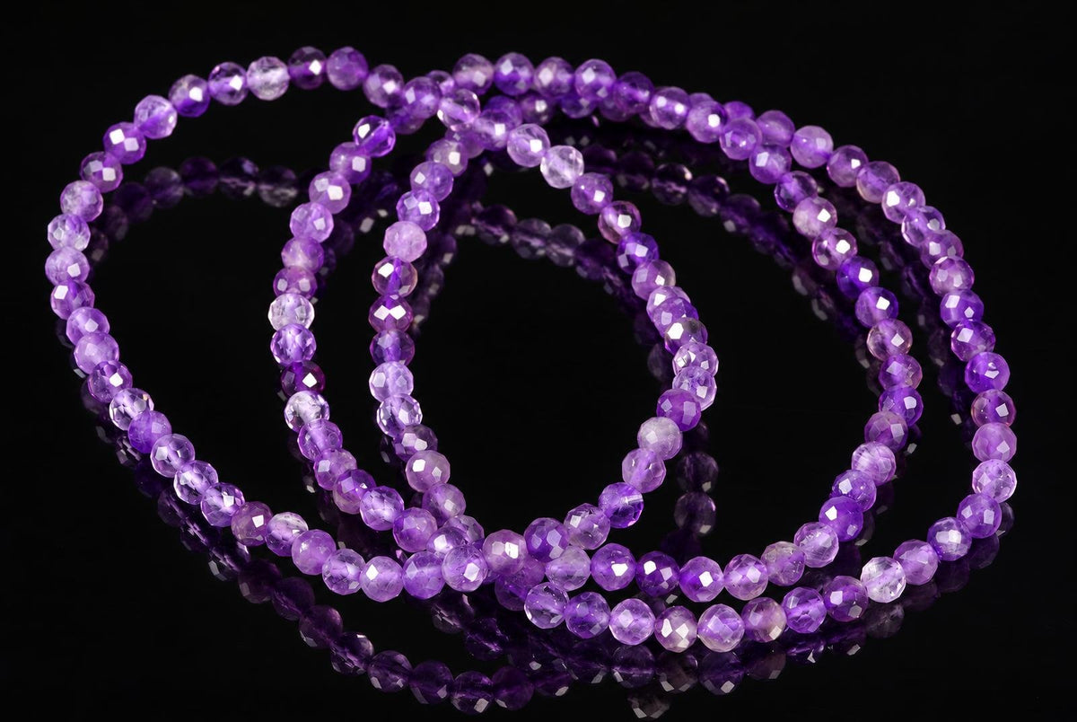 Three strands of faceted purple beads, varying in shade from light to dark, arranged on a dark reflective surface.