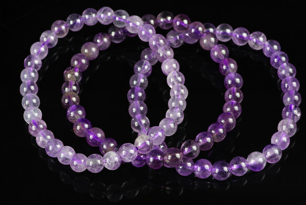 A bracelet of round, translucent purple beads with white inclusions on a dark surface.