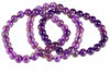 A coiled strand of round, polished purple beads on a white background.