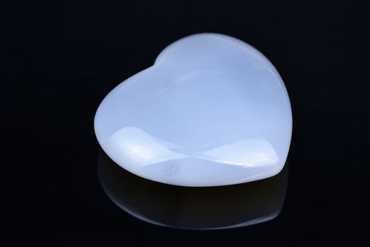 A smooth, heart-shaped object with a pale blue-white surface rests on a dark, reflective surface.