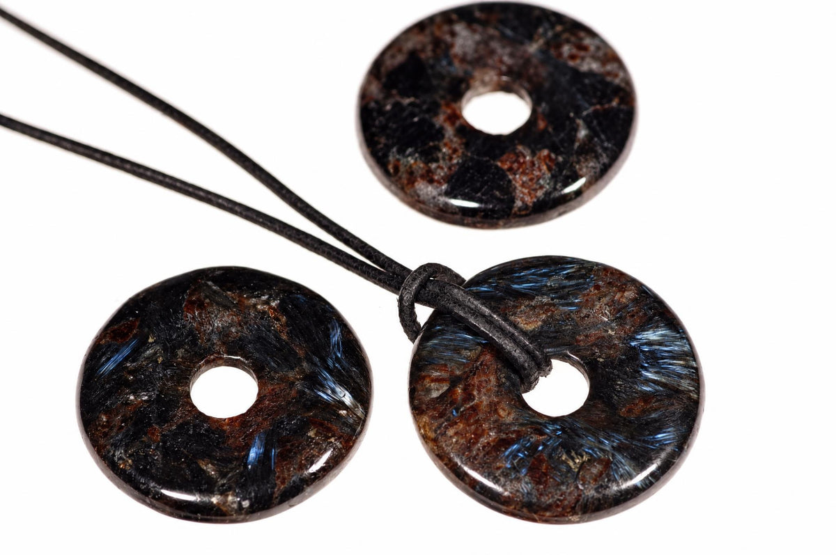 Three dark, polished donut-shaped pendants with blue and brown inclusions on black cords against a white background.