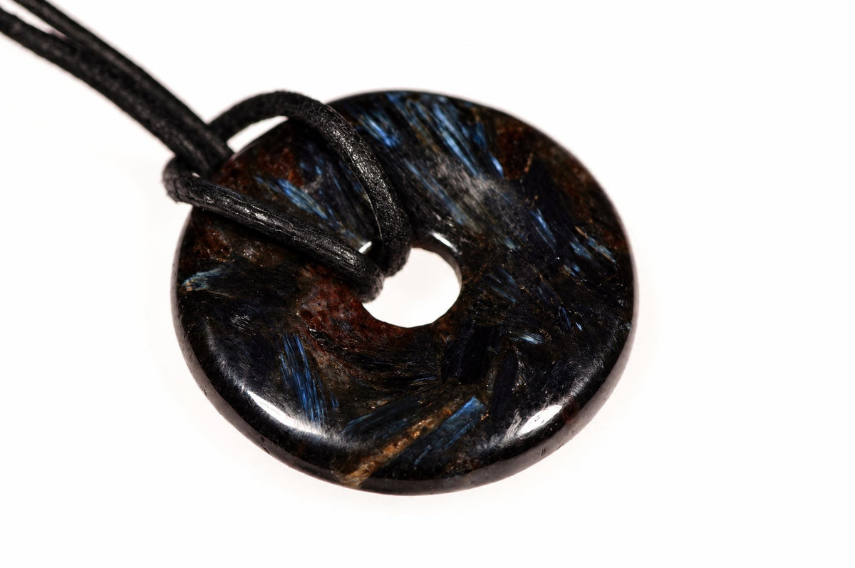 A dark, polished donut-shaped pendant with blue and brown streaks on a black cord against a white background.