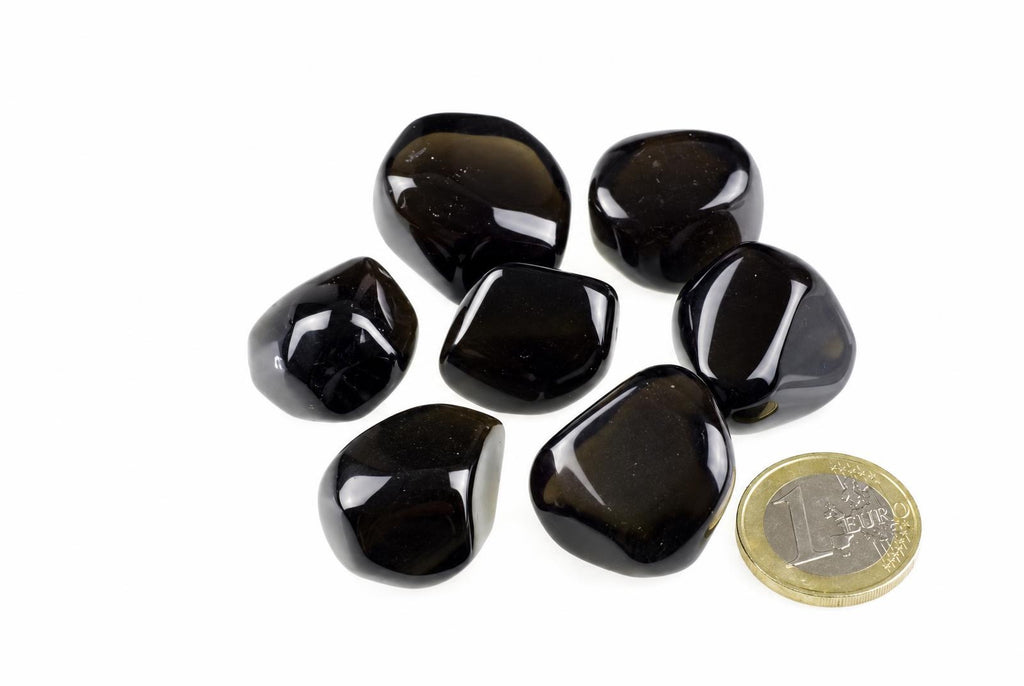 Seven polished dark brown Apache tear stones arranged on a white surface next to a one euro coin.
