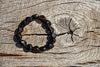 A bracelet of dark brown, polished beads with golden inclusions rests on a weathered wooden surface.