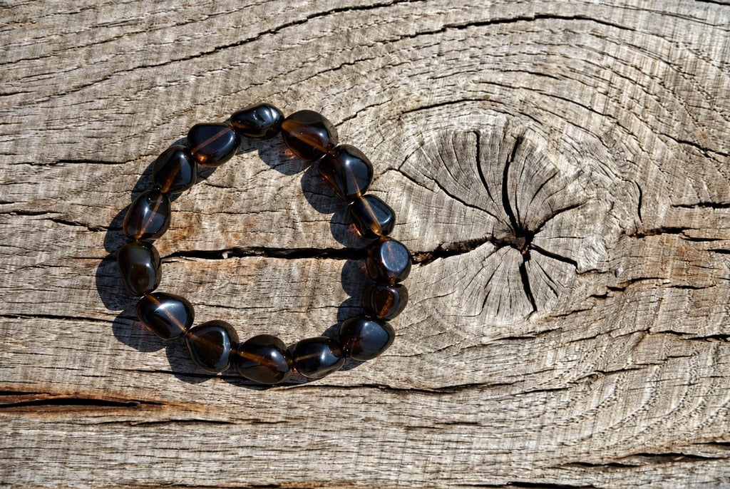 A bracelet of dark brown, polished beads with golden inclusions rests on a weathered wooden surface.
