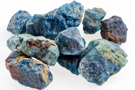 A pile of raw apatite crystals showing blue, green and brown colours on a white surface.