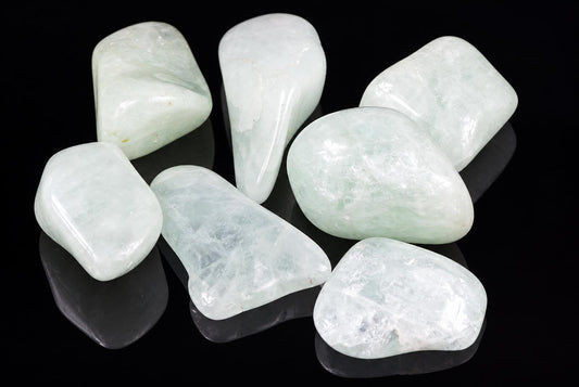 Seven polished aquamarine stones in pale green and white, arranged on a dark reflective surface.
