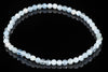 A bracelet of faceted beads in pale blue, white and clear tones arranged on a dark reflective surface.