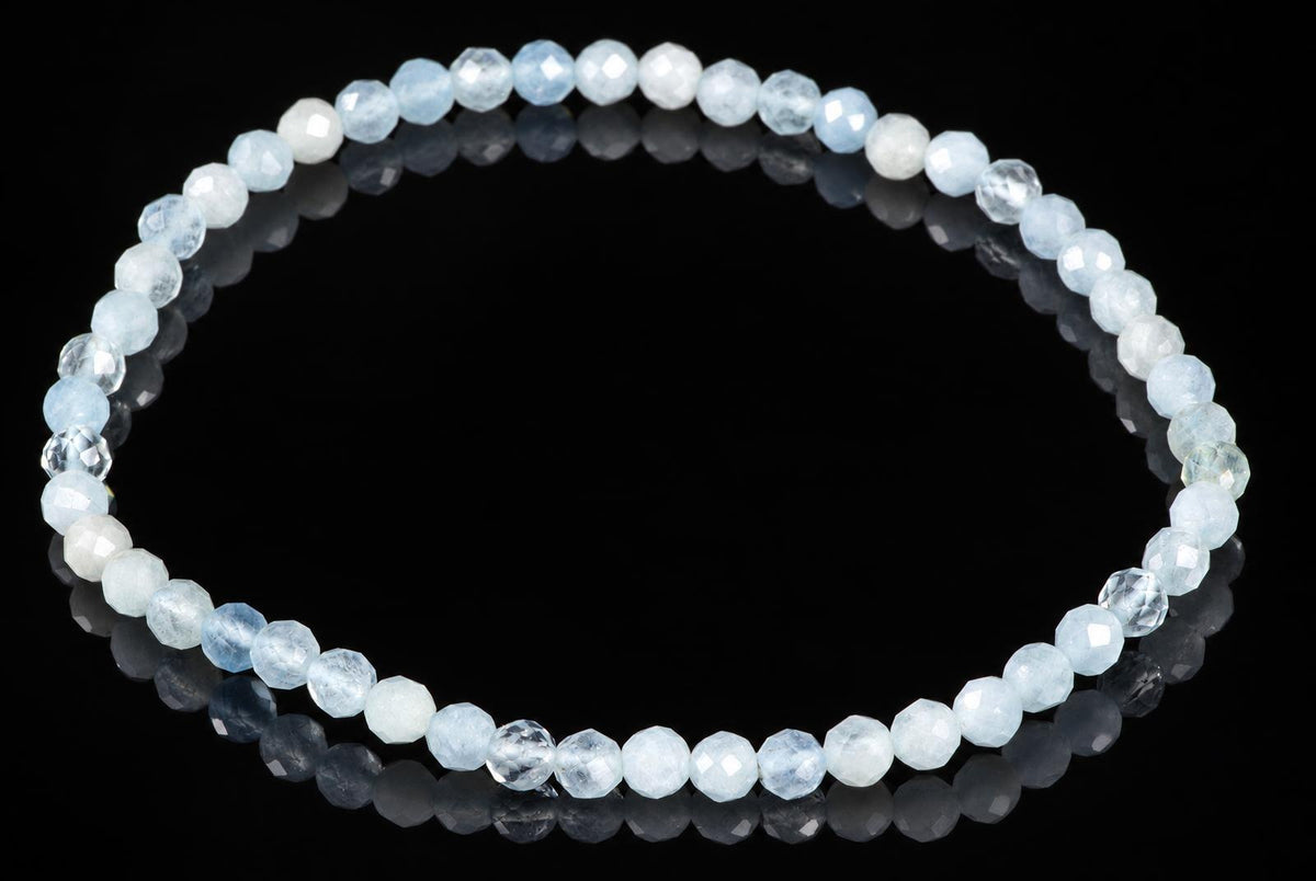 A bracelet of faceted beads in pale blue, white and clear tones arranged on a dark reflective surface.