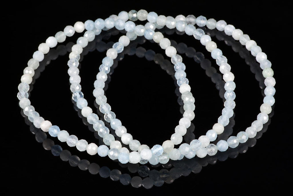 Overlapping bracelets of small faceted pale-blue and milky-white beads rest on a glossy black surface.