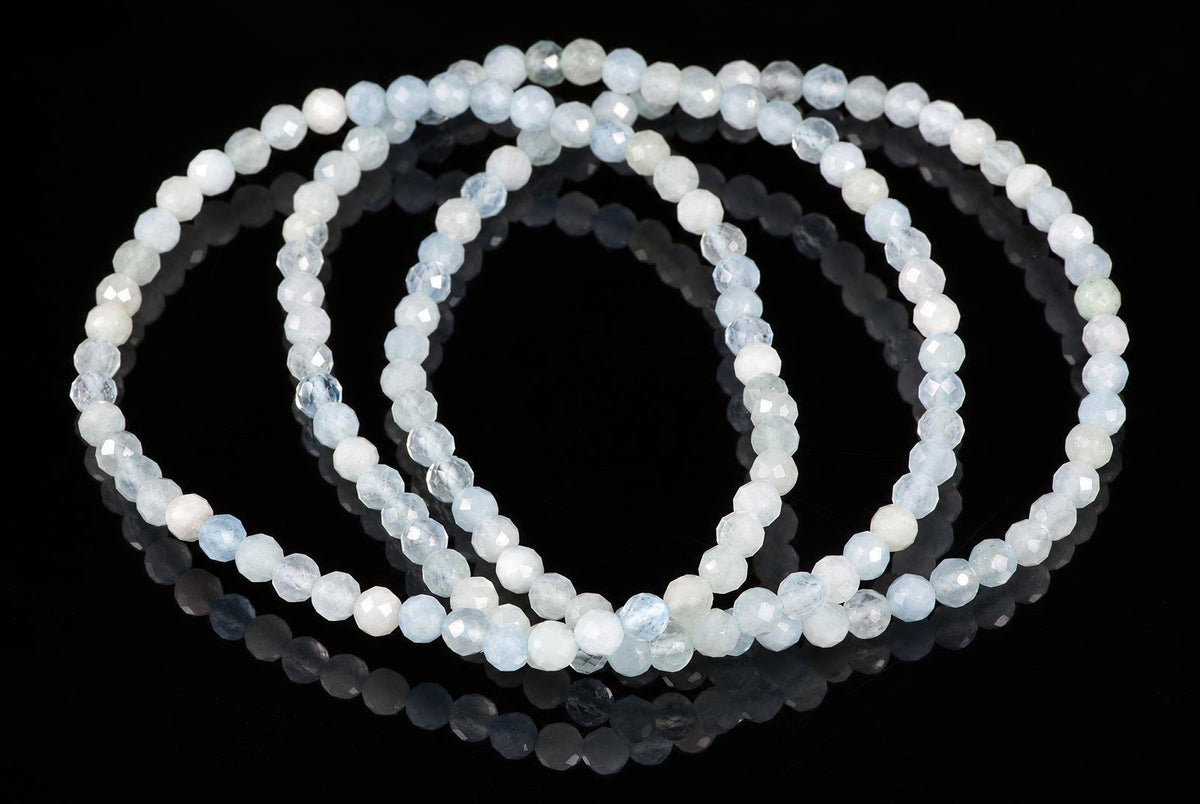Overlapping bracelets of small faceted pale-blue and milky-white beads rest on a glossy black surface.