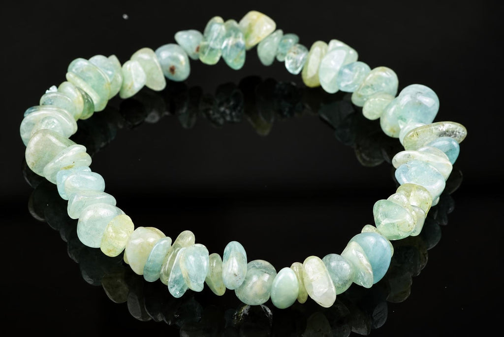 A bracelet made of irregular, polished chips in pale blue, green and white tones on a dark reflective surface.