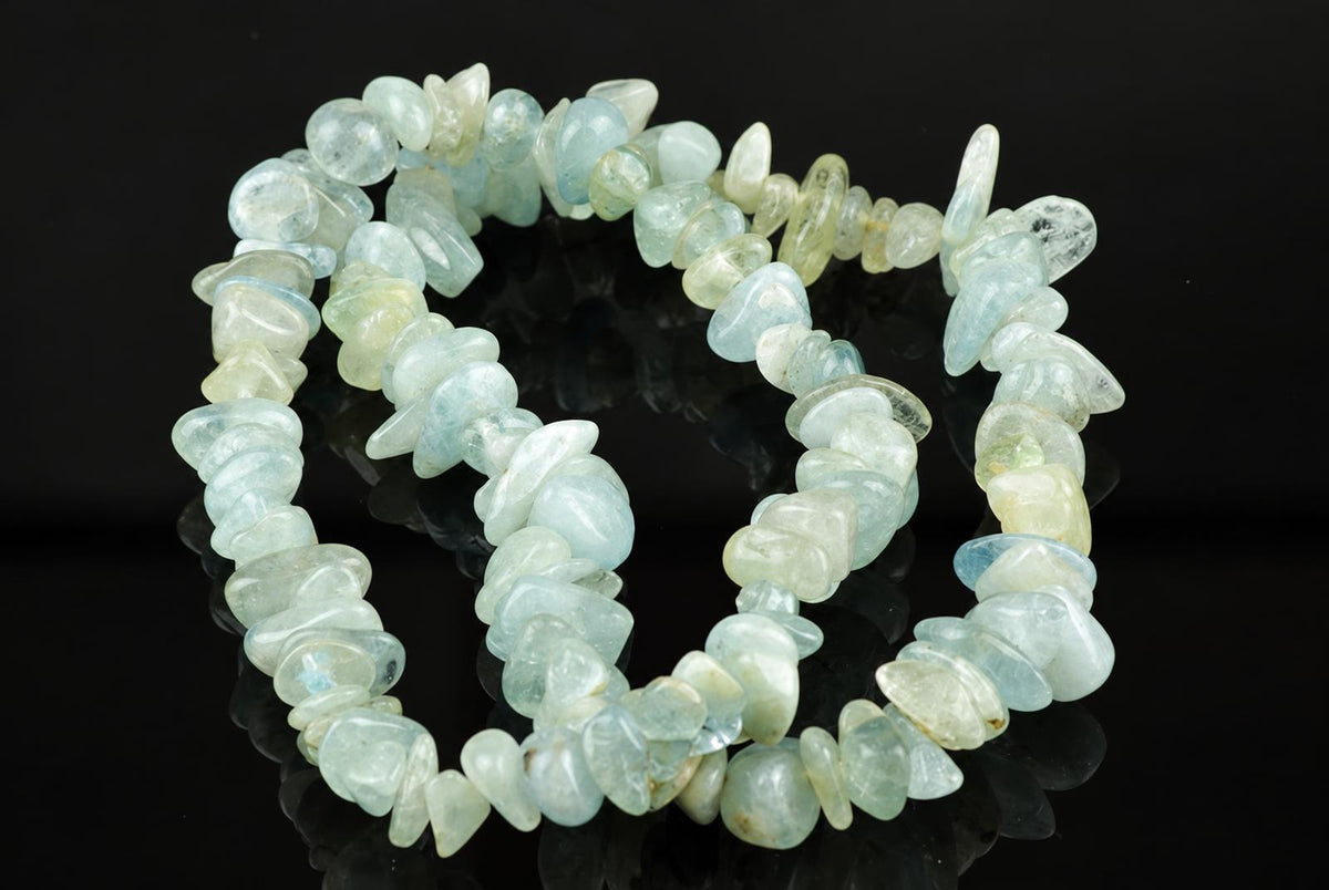 A bracelet made of irregular chips in pale blue, green and white tones on a dark reflective surface.